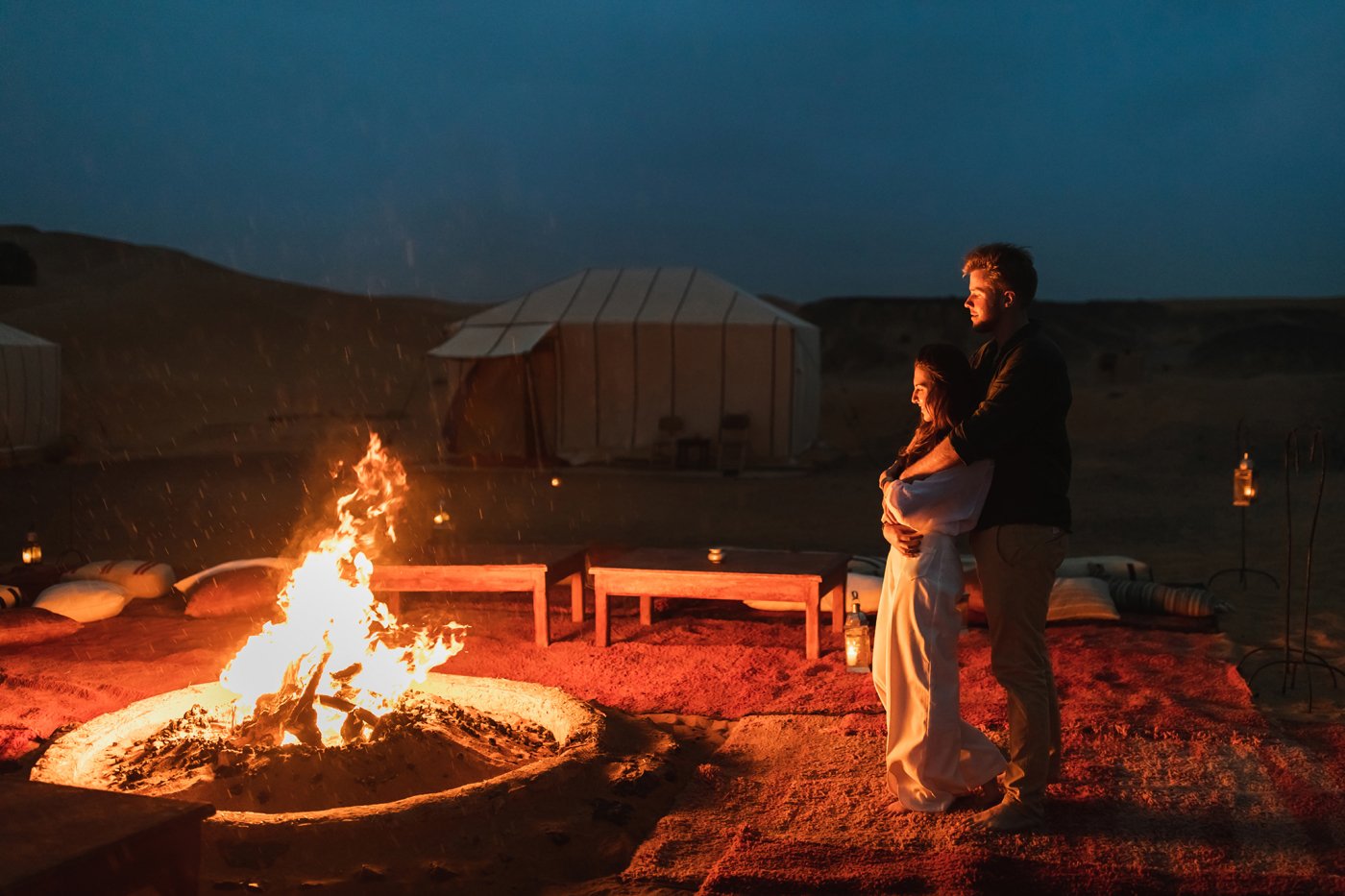 Couple hug in love near big campfire. Romantic night in glamping desert camp in Sahara, Morocco. Honeymoon.