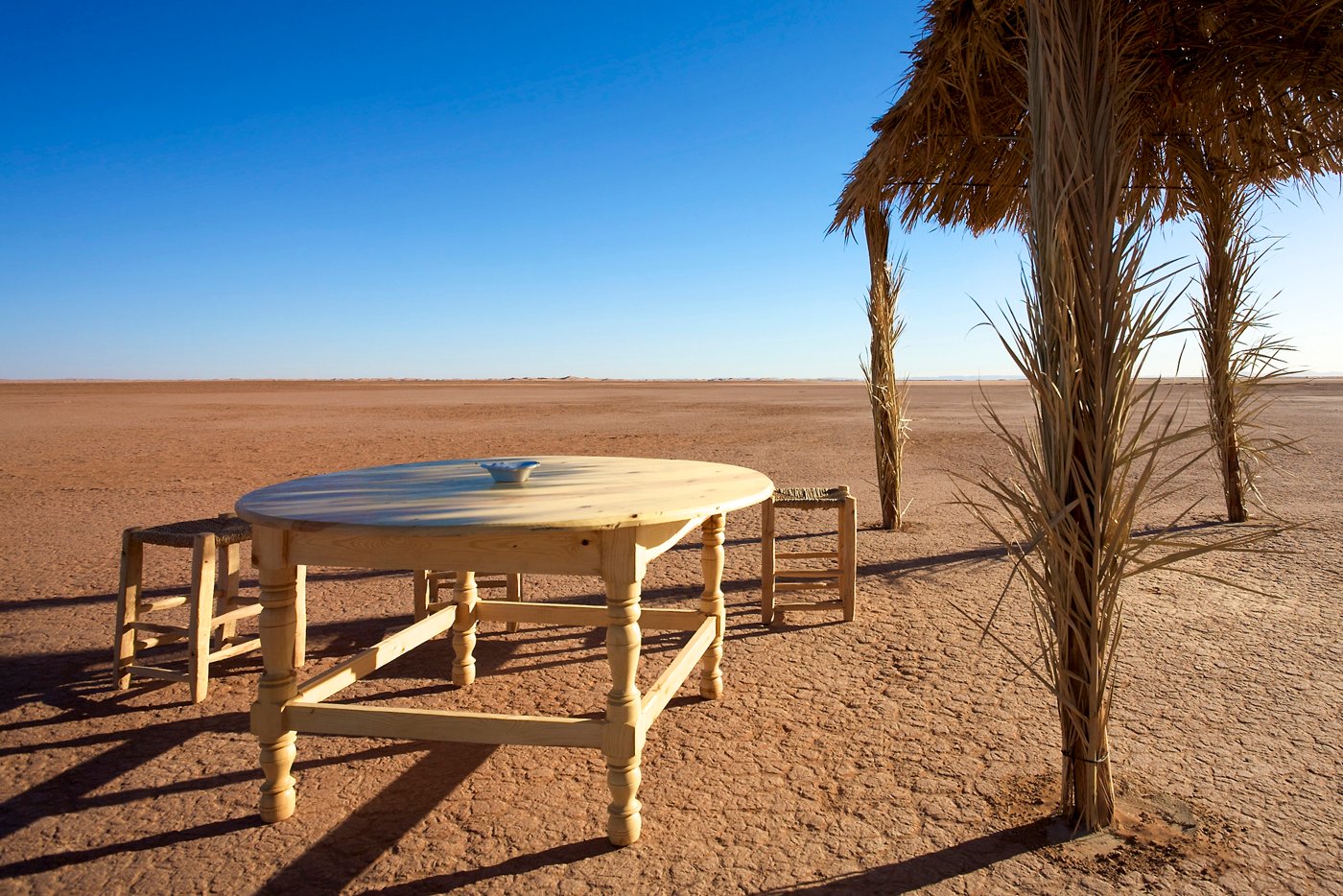 MHAMID, MOROCCO, NOVEMBER 18: View of desert with old wooden chairs and table next to a sun shelter with clear blue sky. Morocco 2010.